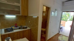 A compact kitchen with a sink, stove, and wooden cabinets. A dining table with a chair is in the foreground. - Apartments Vinko Mljet- One-bedroom Apartment With Terrace (Mljet)