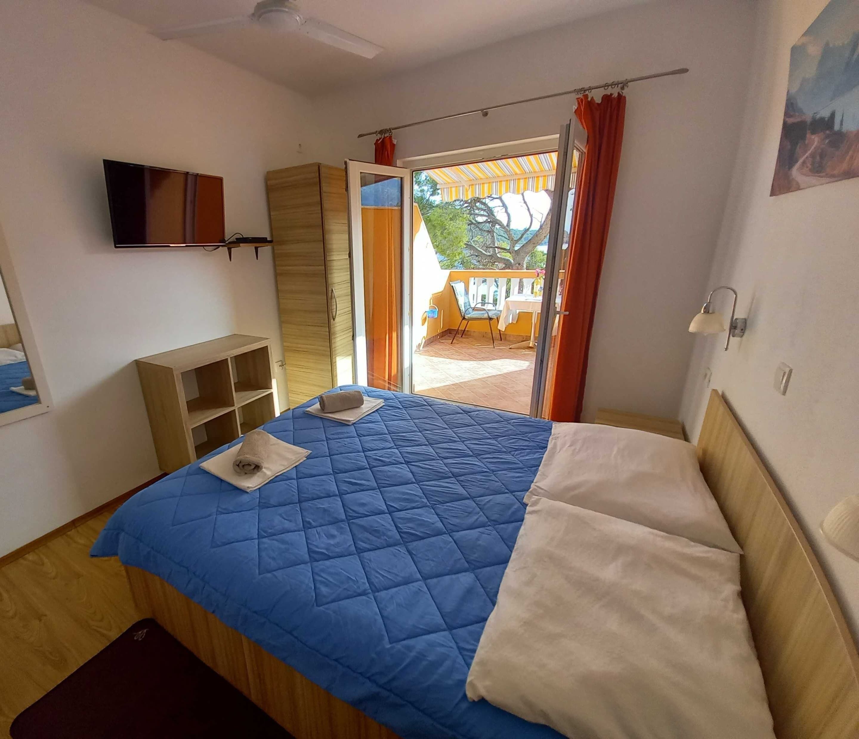 A bedroom with a bed, a TV, a wardrobe, and a view of the outside balcony.