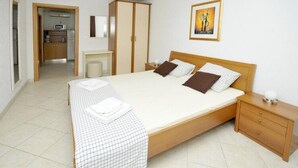 A bedroom with a large bed, a bedside table, a wardrobe, and a kitchenette in the background. - Apartments Villa Moonlight - One Bedroom Apartment With Sea View Balcony and Terrace (Okrug)