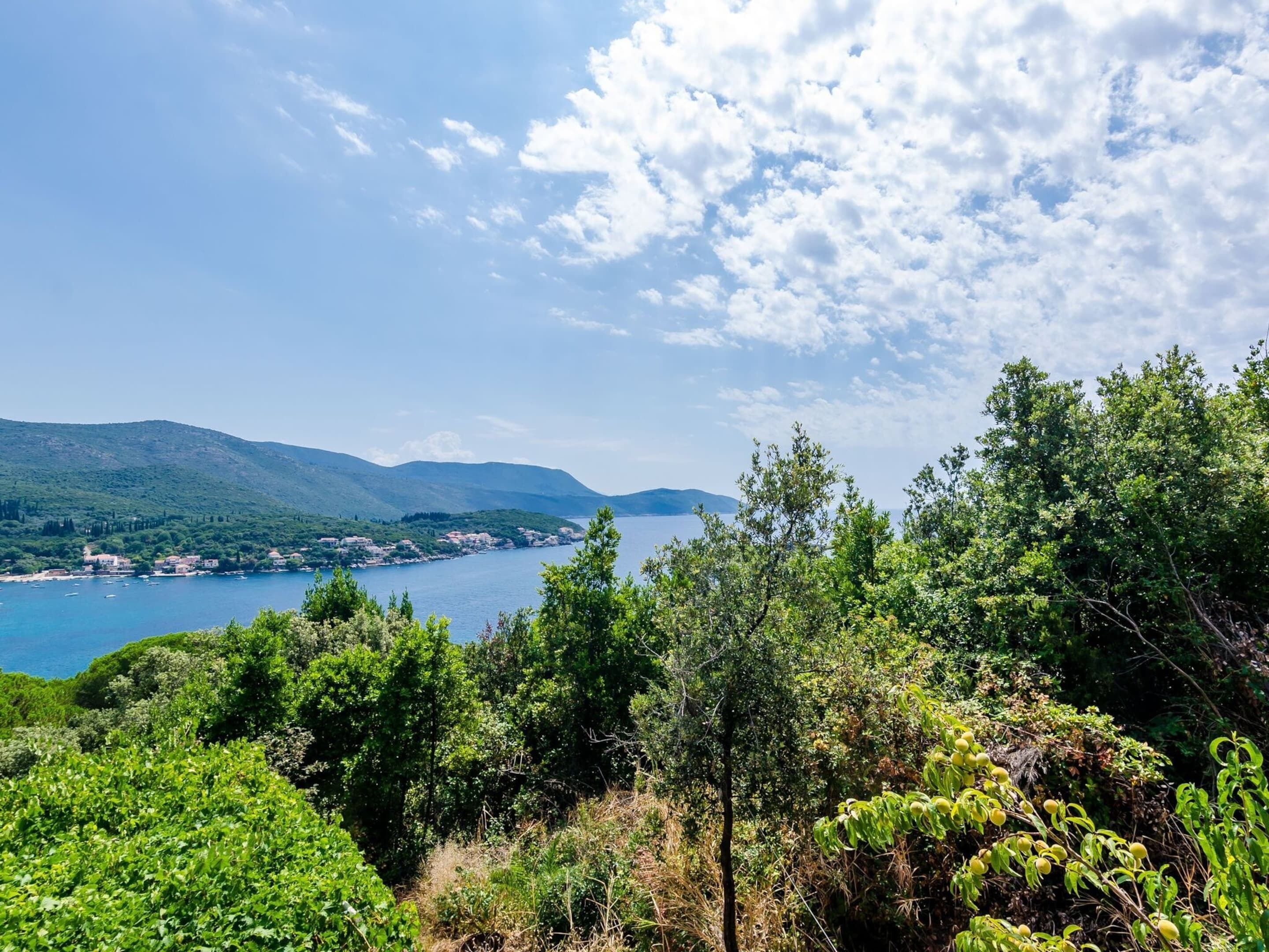 A coastal landscape with a view of the sea, mountains, and dense greenery.