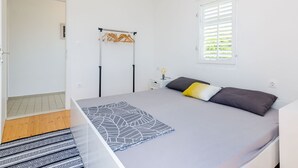 A bedroom with a bed, a window with blinds, a hanging light fixture, and a wardrobe with clothes. - Apartment Konak - Two Bedroom Apartment With Balcony and Sea View (Konavle)