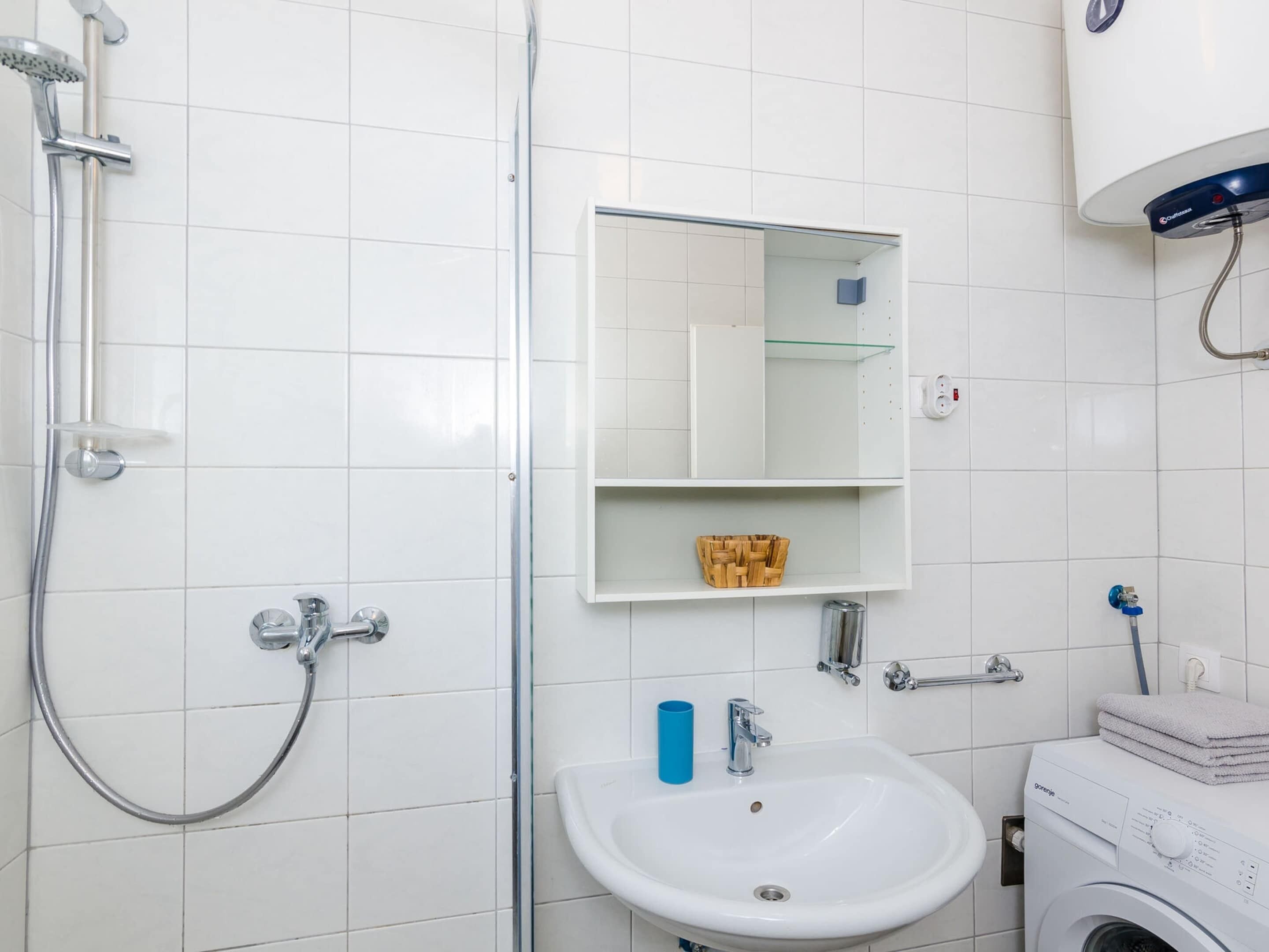 A bathroom with a shower, sink, mirror, and a washing machine.