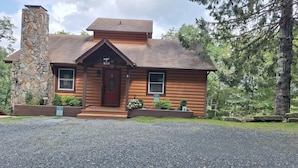 A log cabin with a stone chimney, a front porch, and a small garden.