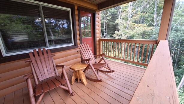 A wooden deck with two rocking chairs and a small table.
