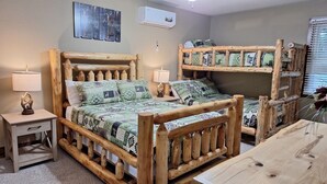 A room with a wooden bunk bed, a bedside table with a lamp, and a wall-mounted air conditioner.
