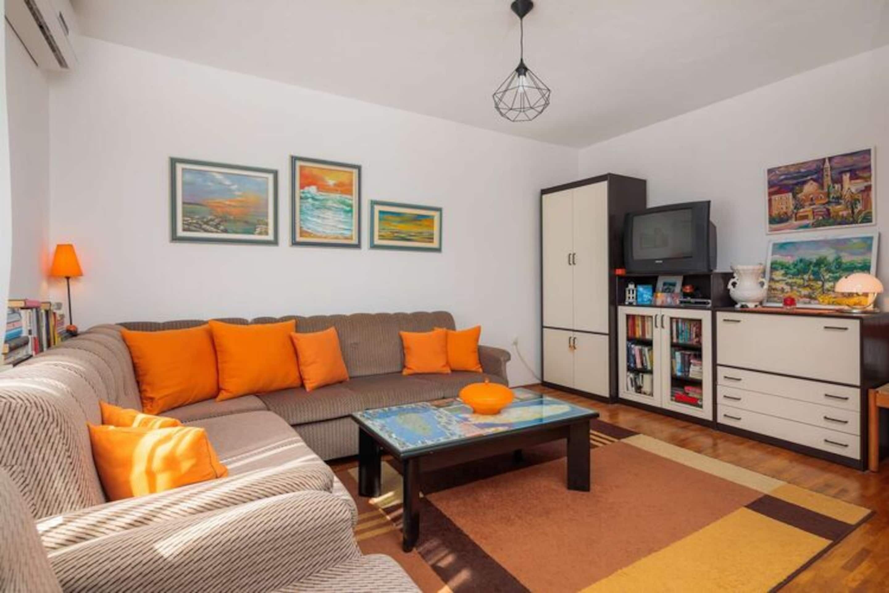 A living room with a sofa, coffee table, and cabinets. There are paintings on the wall and a lamp on the side.