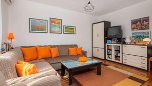 Een woonkamer met een bank, salontafel en kasten. Er hangen schilderijen aan de muur en er staat een lamp ernaast.