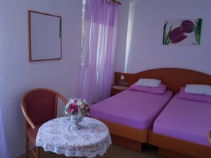 A bedroom with a bed, a chair, a table with a vase of flowers, and a painting on the wall. - Rooms Milena - Double or Twin Room With External Private Bathroom (Dubrovnik)