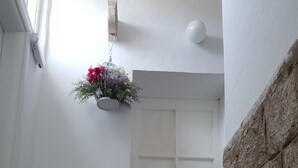 Una puerta blanca con un pequeño ventanal en la parte superior, una planta en maceta a la izquierda y un muro de piedra a la derecha.