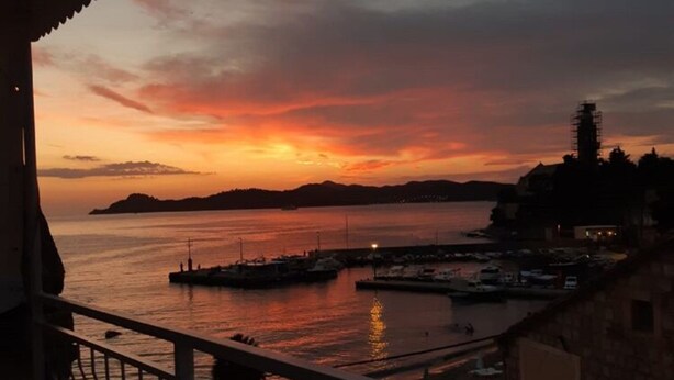 Vista del atardecer desde un balcón con vista a un puerto deportivo con barcos y una isla distante.