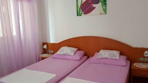 Una habitación con dos camas individuales, cada una con un almohadón blanco y una colcha morada. Hay una mesita de noche con una lámpara a cada lado de las camas. Un cuadro de tulipanes rojos está en la pared sobre las camas.