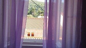 Vista a través de cortinas moradas de un edificio con techo de tejas y una ventana.