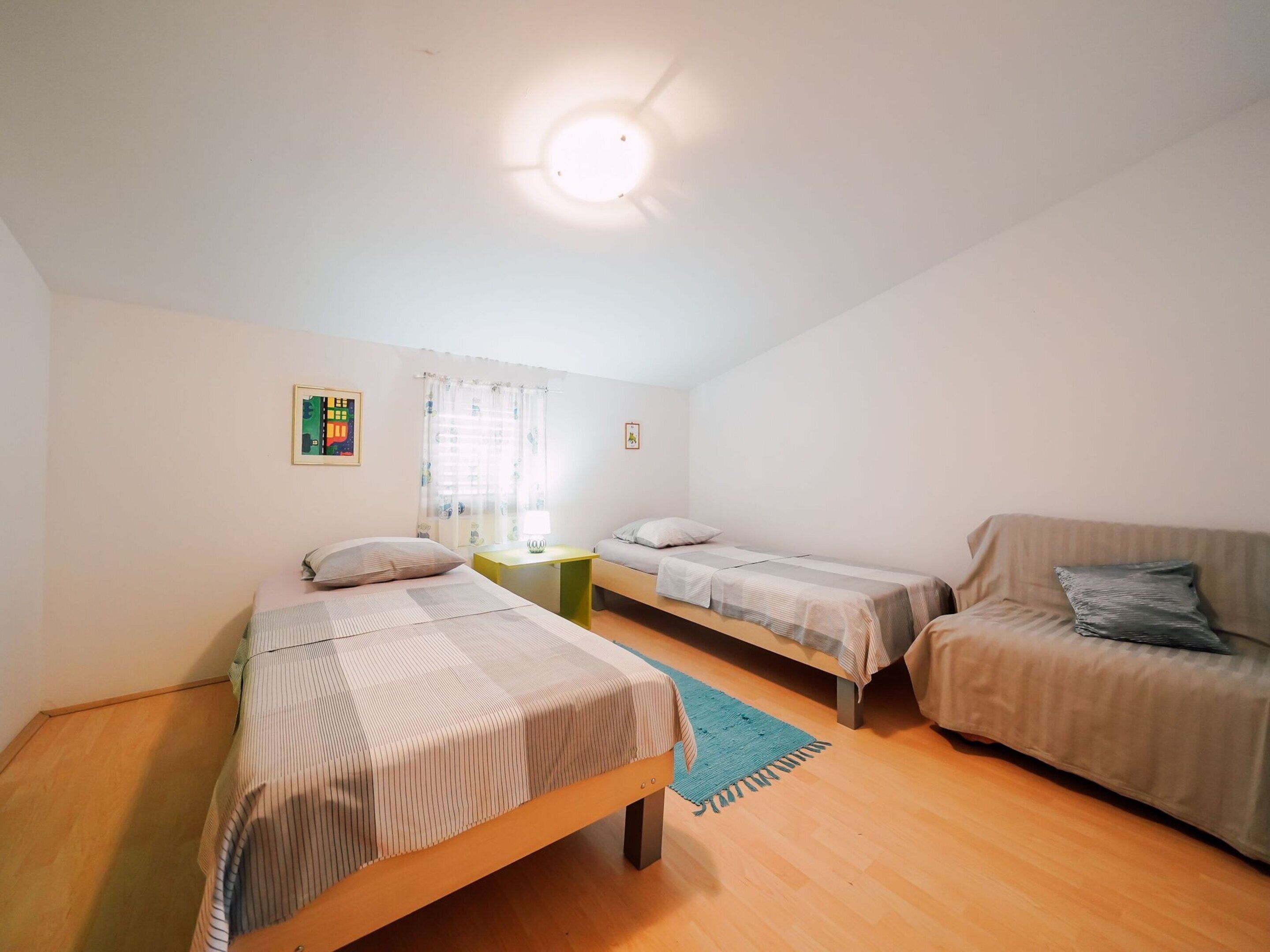 A room with two beds, a small table, a couch, and a ceiling light.