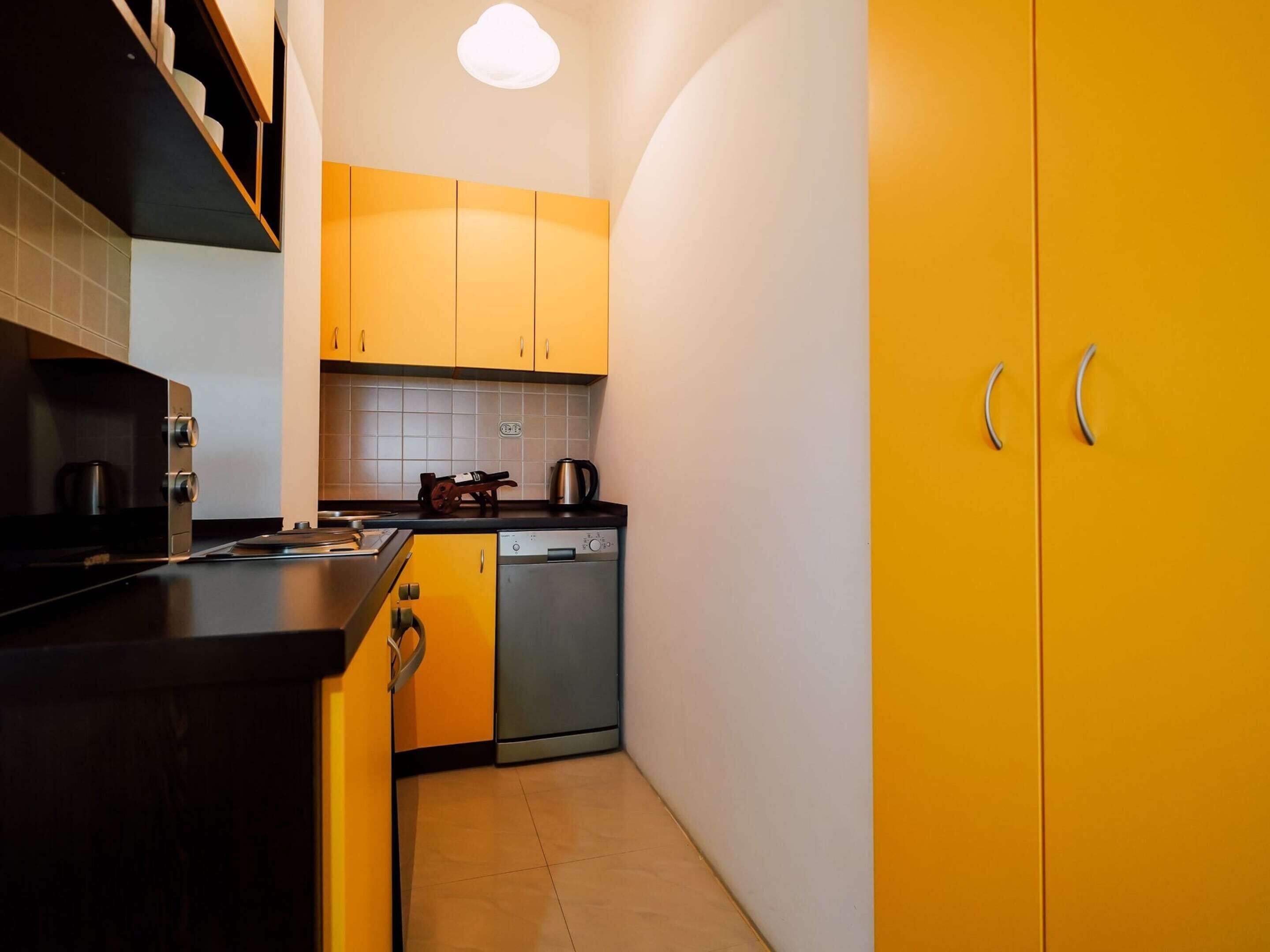 A compact kitchen with yellow cabinets, a dishwasher, and a microwave.
