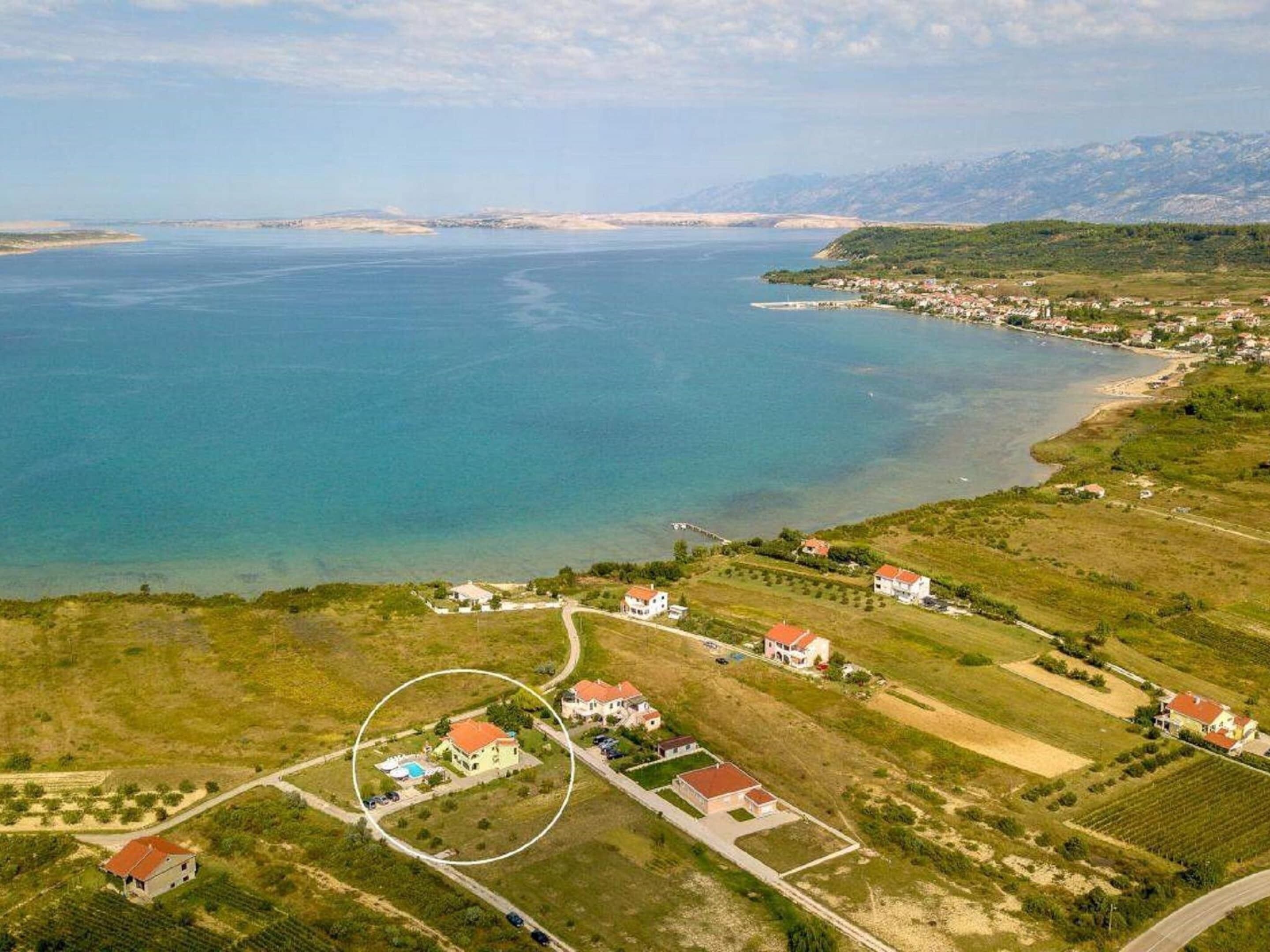 Luchtbeeld van een kustgebied met huizen, een heldere blauwe zee en een bergachtig landschap.