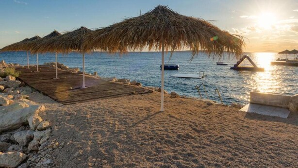 Ein Strand mit Reetsonnenstühlen und einer Holzpromenade, die zum Wasser führt.