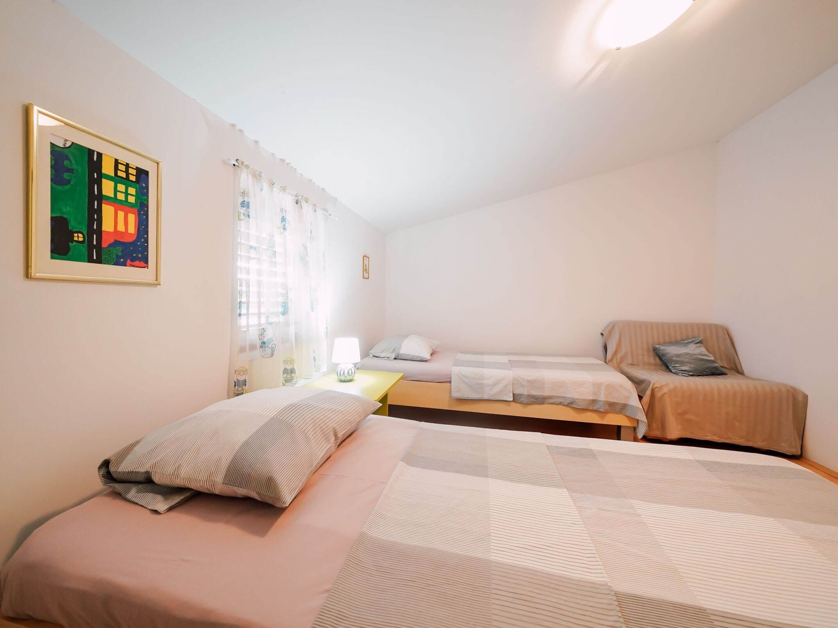 A bedroom with two beds, a small table, a lamp, and a painting on the wall.
