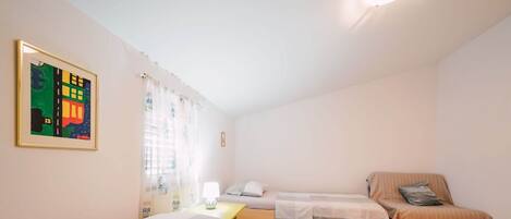 A bedroom with two beds, a small table, a lamp, and a painting on the wall.