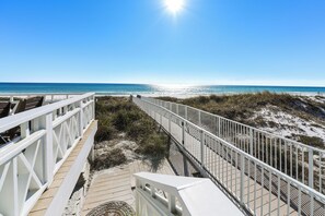 A wooden boardwalk leading to a beach with white railings and a clear view of the ocean.