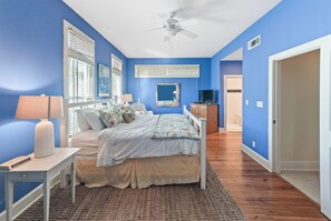 A bedroom with a bed, a ceiling fan, a TV, and a bathroom visible through an open door.