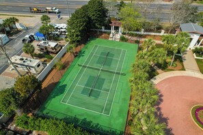 An aerial view of a tennis court surrounded by greenery and a parking area with RVs.