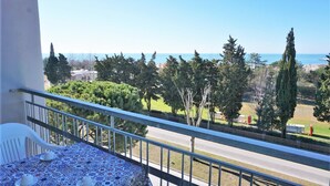 A balcony with a table and chairs, overlooking a coastal area with trees and a road.