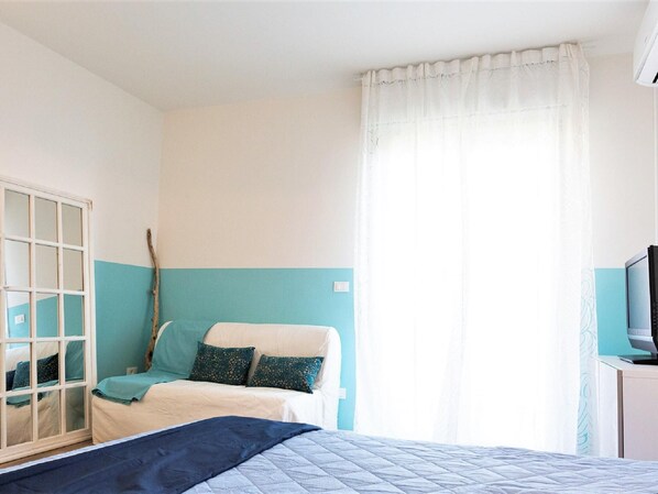 Un dormitorio con cama, armario, televisor y ventana con cortinas.