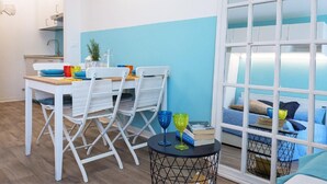 Eine moderne Küche mit weißen Schränken, einer blauen Akzentwand und einem Essbereich mit weißen Stühlen und einem kleinen runden Tisch.