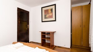 Une chambre à coucher avec un lit, une porte en bois, une armoire en bois, une petite table en bois et un tableau encadré accroché au mur.