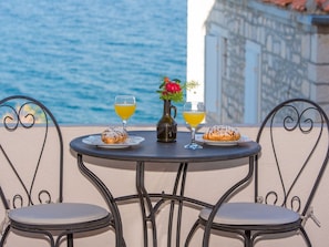 Una mesa con dos sillas, una botella y dos vasos de jugo de naranja, con vista a una masa de agua y un edificio.