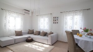 A modern living room with a white sofa, a dining table with chairs, and a large window with patterned curtains. - Apartment Marcela - Deluxe Two Bedroom Apartment With Terrace and Sea View (Sutivan)