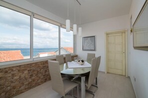Un comedor con una mesa y sillas, vistas al mar a través de amplios ventanales, una pared de piedra y una puerta.