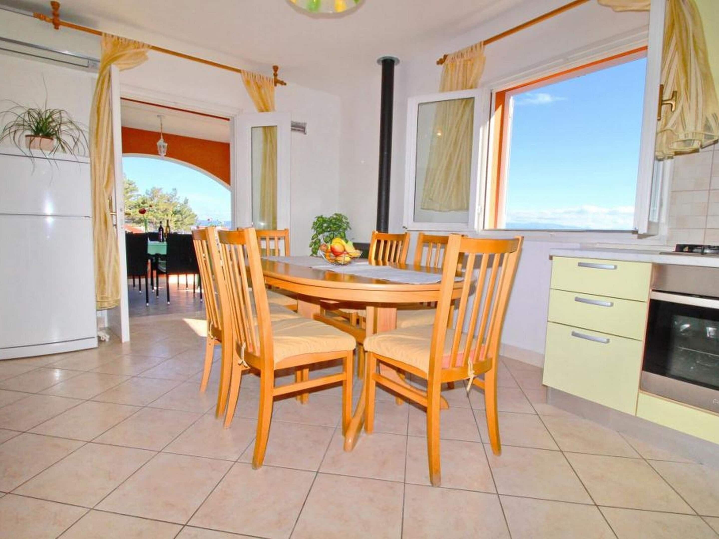 A dining area with a round table and chairs, a kitchen with a stove, and a view through the window.