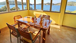 A dining area with a table and chairs, large windows with a view of a lake and hills, and a yellow wall. - Holiday Home Katica - One Bedroom Holiday Home With Terrace and Sea View (Vela Luka)
