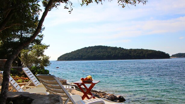 A lakeside view with lounge chairs and a table with fruit, surrounded by rocks and trees. - Holiday Home Katica - One Bedroom Holiday Home With Terrace and Sea View (Vela Luka)
