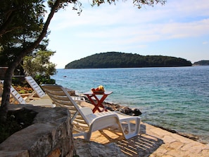 A lakeside view with lounge chairs and a table with fruit, surrounded by rocks and trees.