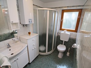 A bathroom with a sink, toilet, shower, and a window.