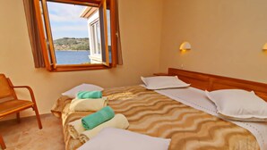 A neatly made bed with a patterned bedspread and pillows, a wooden chair, and a window with a view of the sea. - Holiday Home Katica - One Bedroom Holiday Home With Terrace and Sea View (Vela Luka)