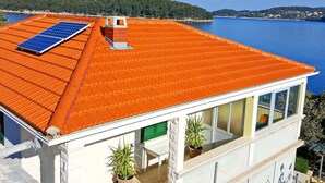 A modern building with a red-tiled roof, a solar panel, and a view of a lake and forest. - Holiday Home Katica - One Bedroom Holiday Home With Terrace and Sea View (Vela Luka)