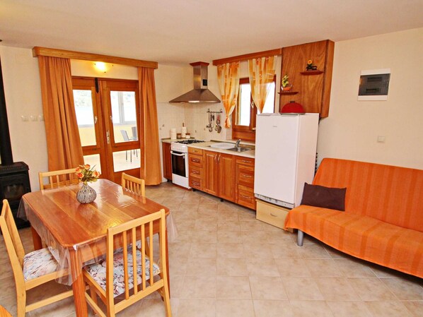 A compact kitchen with wooden cabinets, a gas stove, a white refrigerator, and a dining area with a wooden table and chairs.