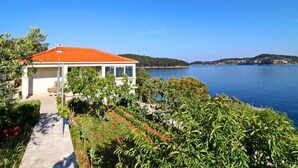 A coastal house with a red roof, surrounded by lush greenery and a clear blue sea. - Holiday Home Katica - One Bedroom Holiday Home With Terrace and Sea View (Vela Luka)