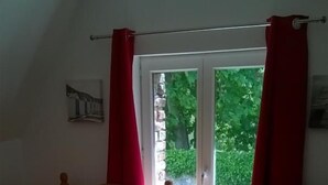 Ett sovrum med två sängar i trä, en röd lampa och ett fönster med röda gardiner.
