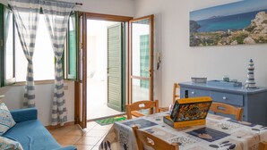 Een kamer met een blauwe bank, een tafel met een tafelkleed met een nautisch thema, een houten kast en een schilderij van een kustlandschap.