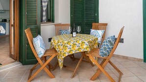 Een eettafel met een tafelkleed met bloemenprint, vier houten stoelen en een fles wijn op de tafel.