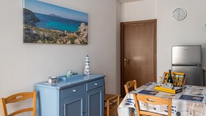 Een eetgedeelte met een tafel gedekt voor twee personen, een blauwe kast en een schilderij van een kustlandschap.