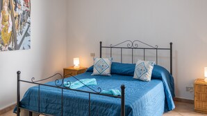 Een bed met een blauwe sprei, twee bijpassende kussens en een metalen frame. Er zijn twee nachtkastjes met lampen.