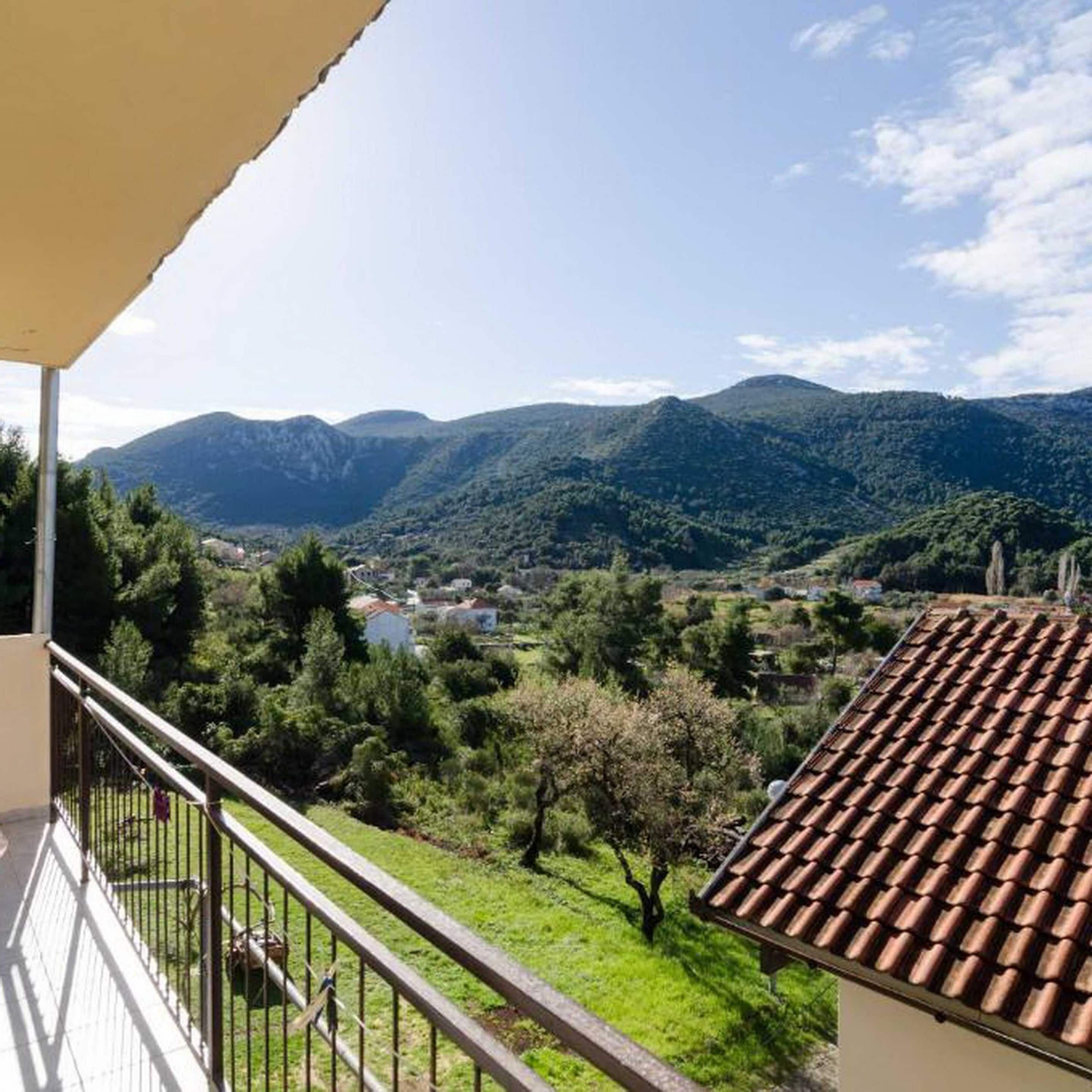 A balcony with a view of a mountainous landscape, a tiled roof, and a grassy area with trees.