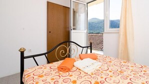 A room with a bed, a window with a view of mountains, and a wooden door.