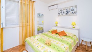 A bedroom with a bed, two bedside lamps, a window with blinds, a wall-mounted air conditioner, and a painting. - Rooms Rita - Double Room With Private Bathroom No. 2) (Dubrovnik)