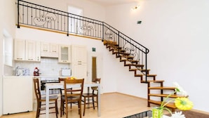 A kitchen with white cabinets, a dining table with chairs, and a staircase with a decorative railing. - Apartments Nikola - Comfort One Bedroom Apartment With City View (Dubrovnik)